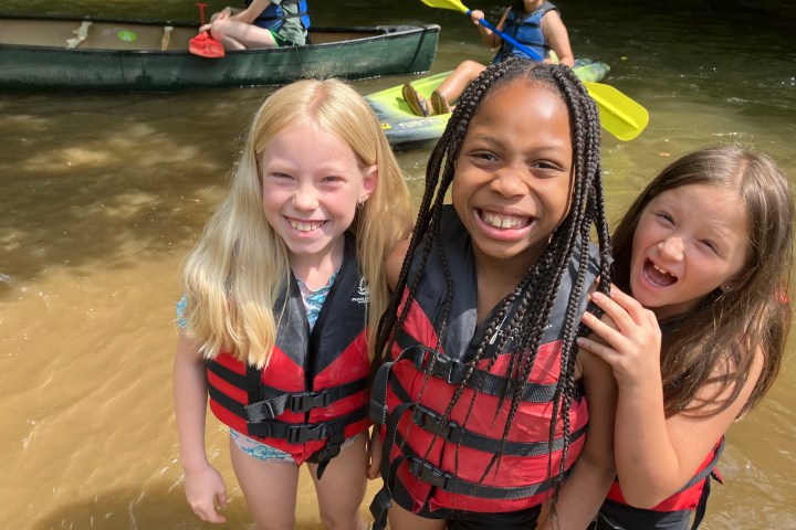 a couple of little girls standing next to a body of water